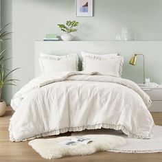 a bed with white comforter and pillows in a room next to a potted plant