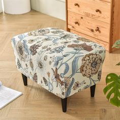 a small footstool sitting on top of a wooden floor next to a plant