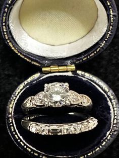 two wedding rings in an open box on a black surface with gold trimmings