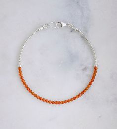 Indulge in the fiery beauty of Carnelian, the orange variety of quartz known for enhancing passion, love, and desire. This stone is also believed to bring confidence, prosperity, and good luck, as well as promote fertility, improve circulation, and alleviate depression. This bracelet is handmade with tiny, smooth polished round Carnelian gemstones surrounded by gold or silver beads. It is available in sterling silver or 14k gold fill. Stone Size: average 2mmStone Bar Length: 3" (7.6cm) Orange Beaded Bracelets, Orange Carnelian, Carnelian Bracelet, Carnelian Beads, Improve Circulation, Energy Stones, Nature Bracelets, Light Orange, 14kt Gold