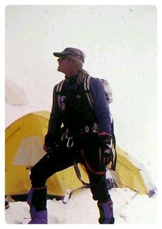 a man standing in the snow next to a yellow tent and some tents behind him