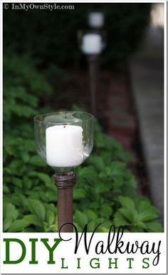 a white candle sitting on top of a wooden pole in front of green plants and bushes