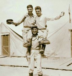 two men and a young boy are standing in front of a tent while one man is holding an infant on his shoulders