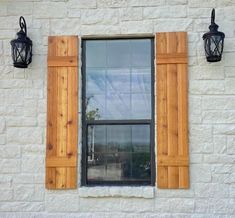 two black lanterns are on the side of a white brick building with wooden shutters