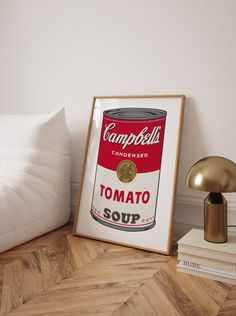 a framed campbell's soup can sits on the floor next to a lamp