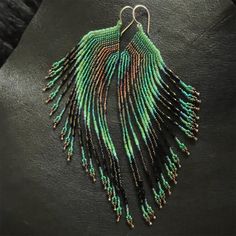 a pair of green and black beaded earrings on top of a leather surface,