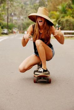 a woman riding a skateboard down a street with a hat on top of her head