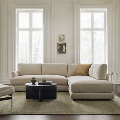 a living room filled with furniture and two large windows in the wall behind it is a coffee table