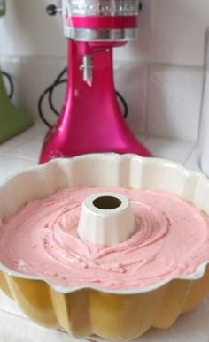 a cake pan filled with pink icing next to a stand mixer on a counter