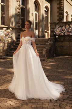 a woman in a white wedding dress standing on the ground near some stairs and flowers