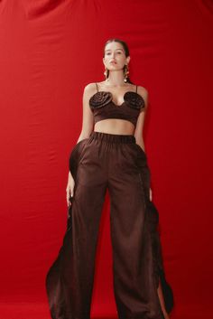 a woman standing in front of a red backdrop wearing brown pants and crop top with cut outs