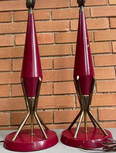 two red and gold lamps sitting on top of a table next to a brick wall