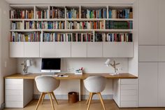 two white chairs sitting at a desk in front of a book shelf filled with books