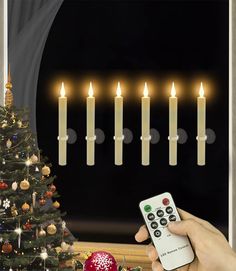 a person holding a remote control in front of a christmas tree with candles on it