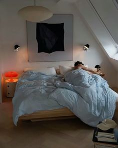 a person laying in bed under a painting on the wall next to a lamp and some books