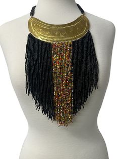 This authentic African necklace boasts a beautiful orange beaded design with tassel fringe accents. The intricate brass pendant adds a touch of elegance to this statement piece, making it the perfect addition to your ethnic jewellery collection. The necklace has been expertly crafted in Africa and showcases the vibrant and unique culture of the region. It is ideal for those who love to add ethnic and tribal styles to their wardrobe. Material:  Beads and decorative brass metal. Fringe - 9ins/22cm Unique Culture, Brass Pendant Necklace, African Necklace, Tassel Fringe, Brass Pendant, Bead Designs, Brass Metal, Jewellery Collection, Black Beads