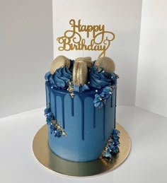 a birthday cake with blue frosting and gold decorations on top, sitting on a white table