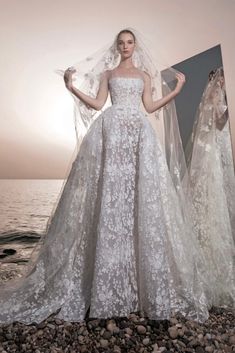 a woman in a wedding dress standing on rocks near the ocean with her veil over her head