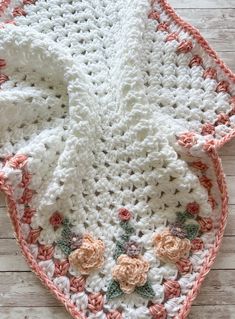 a crocheted blanket with flowers on it sitting on top of a wooden floor