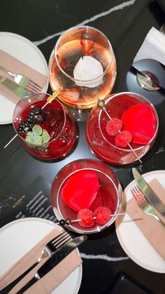 three glasses filled with red liquid on top of a table next to plates and utensils