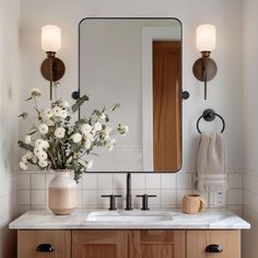 a bathroom vanity with flowers in a vase on the counter and two mirrors above it