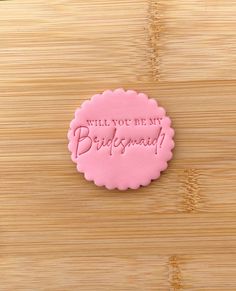 a pink cookie that says will you be my bridesmaid?