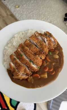 a white plate topped with rice and meat covered in gravy on top of a table