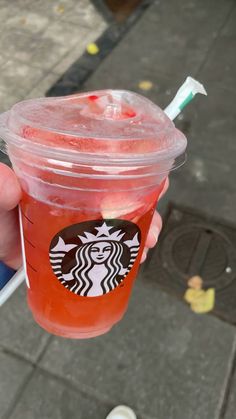 a person holding up a plastic cup with a drink in it's hand on the sidewalk