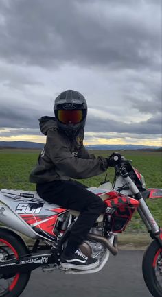 a man riding on the back of a motorcycle down a road next to a lush green field