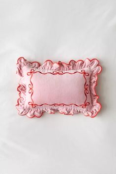 a pink and red decorative pillow on a white bed with ruffle trimmings