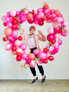 a woman standing in front of a bunch of pink and red balloons on top of a white wall