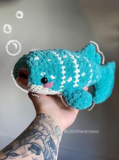 a hand holding a small blue and white crocheted fish with bubbles coming out of it's mouth