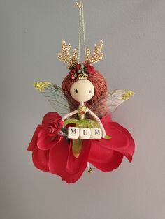 a red flower with a doll hanging from it's side and the word mum spelled in white letters