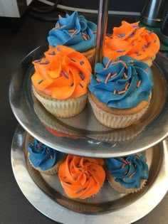 cupcakes with blue and orange frosting are on three tiered trays