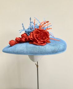 "A stunning pale blue and orange wide brim hatinator.  This gorgeous statement headpiece is made using sinamay straw in a beautiful shade of powder blue. Central to this hat, is a  large handmade silk dupion rose in burnt orange and five matching rose buds that cascade down the brim to one side.  A small collection of powder blue and orange feathers float out  from the top of the rose, adding movement and drama to the overall finished hat.  This particular design has a shallow brim and is secured with a double metal headband that it ribbon wrapped in a colour to blend in with your own hair colour. This band is completely invisible when the hat is on.  Measuring 44cm side to side and 37cm front to back. It is made to a standard 22\" diameter, however, if you require a smaller fit I can prov Summer Blue Headpiece With Handmade Flowers, Blue Costume Hats And Headpieces For Races In Spring, Blue Fascinator With Curved Brim For Spring, Blue Curved Brim Fascinator For Spring, Blue Curved Brim Headpiece For Royal Ascot, Spring Blue Fascinator With Curved Brim, Blue Fascinator With Handmade Flowers For Kentucky Derby, Blue Handmade Flowers Fascinator For Races, Blue Fascinator For Royal Ascot Garden Party