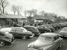 an old black and white photo of cars parked in a parking lot with people standing around