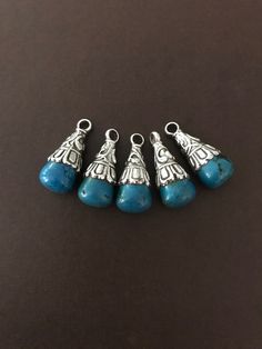 five silver and turquoise beads on a black surface