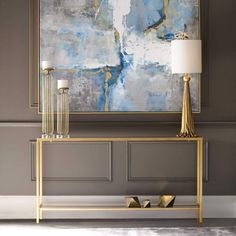 an abstract painting hangs on the wall above a console table with two lamps in front of it