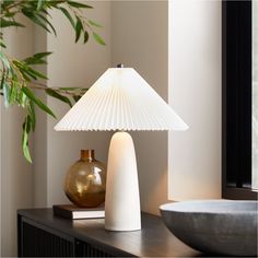 a white lamp sitting on top of a wooden table next to a bowl and vase