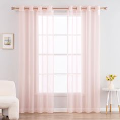 a white chair sitting in front of a window covered in pink sheer curtaines and flowers