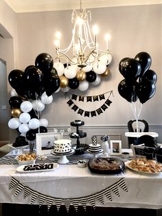 a table topped with lots of balloons and desserts next to a chandelier