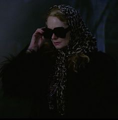 a woman wearing sunglasses and a leopard print scarf is talking on her cell phone in the dark