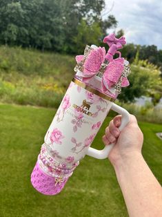 a person holding a coffee mug with pink flowers and bows on the inside, in front of a grassy area