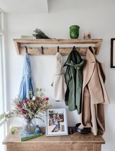 a wooden shelf with coats hanging from it's hooks and pictures on the wall