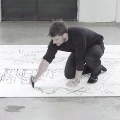 a man kneeling down on top of a white floor next to an apple pencil drawing