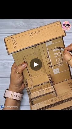 two hands are holding open cardboard boxes with drawings on them and one hand is pointing at the box