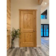 a wooden door in a white room with wood flooring and large windows on the wall