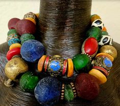 Look at the vibrant colors in this bold, chunky, heavy and oversized beaded African - Tibetan beaded two strand statement necklace! This features African recycled glass, Yoruba brass, Zebu bone disks and beads, Moroccan resin, Nepalese glass, metal daisy spacers, Tibetan resin and Tibetan fancy inlaid beads, tribal metal spacers and fancy silver tone etched or stamped beads. Adjusts from 17-20" with gold tone hardware, a lobster claw clasp, and a 3" extender chain with a ethnic heart pendant. Pl Bold Multicolor Beaded Necklaces, Eclectic Multicolor Beaded Bracelets With Wooden Beads, Eclectic Multicolor Wooden Beaded Bracelets, Eclectic Multicolor Beaded Necklaces With Large Beads, Traditional Colorful Large Beads, Eclectic Multicolor Beaded Necklace With Large Beads, Festive Multicolor Large Beads, Festive Large Multicolor Beads, Multicolor Festive Beads