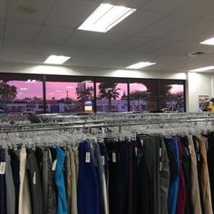 clothes are hanging on racks in front of large windows at an office building as the sun sets