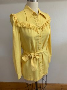 "Sweet yellow blouse, designed to be worn untucked, with a tie at waist that can be tied in front or back. Sweet crochet lace trim at cuffs and yoke. Western detailing. Not sure of the fiber content but it feels like a poly blend, but it has the look of a raw silk loose weave. Laid flat it measures- Shoulder to shoulder 14.5\" Pit to pit 19\" Neck 8\" Waist 16\" Hip 19\" Front length 26\" Model is 5'8\" size 6 for reference Please ask any questions prior to purchase and see all photos, all sales Yellow Tops With Crochet Trim For Spring, Fitted Long Sleeve Blouse With Crochet Trim, Vintage Crochet Trim Tops For Spring, Spring Crochet Trim Blouse, Vintage Tie Neck Tops For Spring, Fitted Yellow Blouse For Daywear, College Clothes, Blouse Designed, Crochet Lace Trim